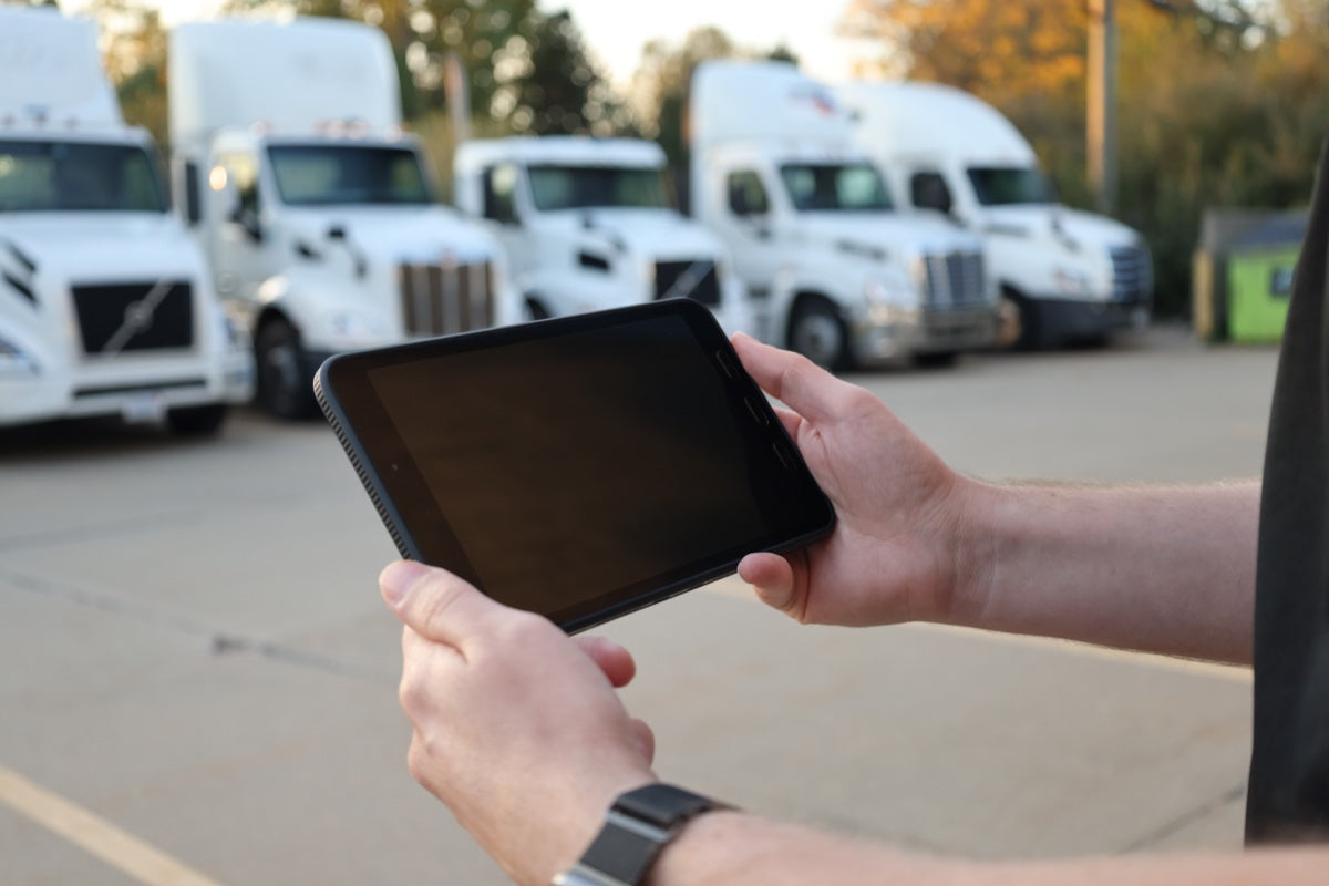 Samsung Galaxy Tab Active5 tablet held in front of a row of semi trucks